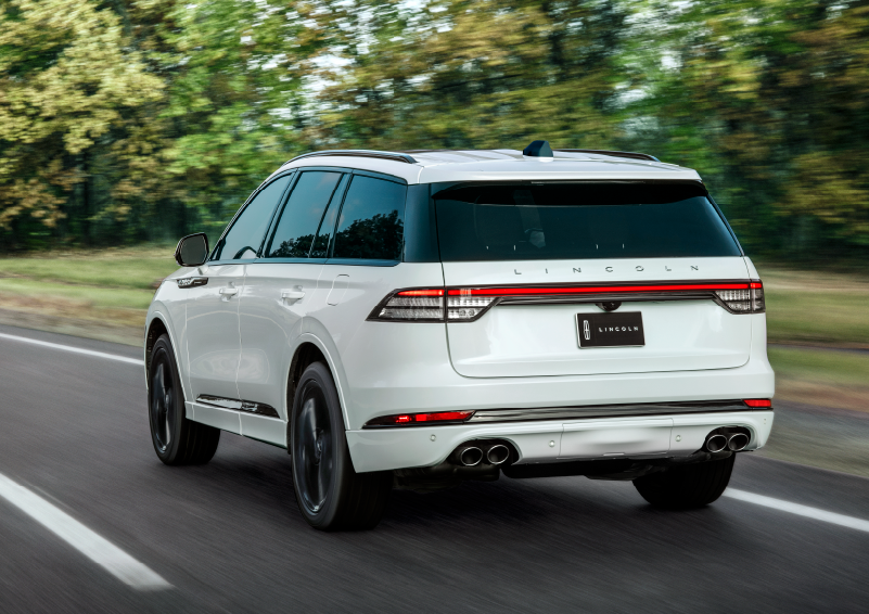 A white 2025 Lincoln Aviator® SUV is being driven away down a road lined with colorful trees. | Parks Lincoln of Wesley Chapel in Wesley Chapel FL
