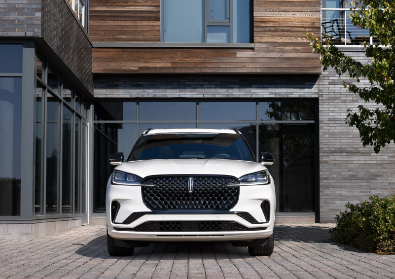 A white 2025 Lincoln Aviator® SUV is shown parked outside a modern building with gray brick and wood accents. | Parks Lincoln of Wesley Chapel in Wesley Chapel FL