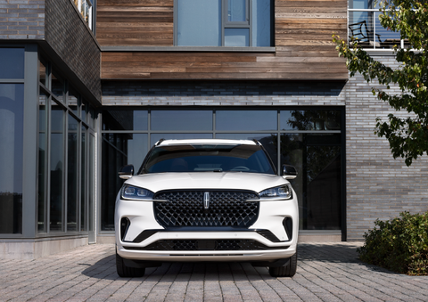 A white 2025 Lincoln Aviator® SUV is shown parked outside a modern building with gray brick and wood accents. | Parks Lincoln of Wesley Chapel in Wesley Chapel FL