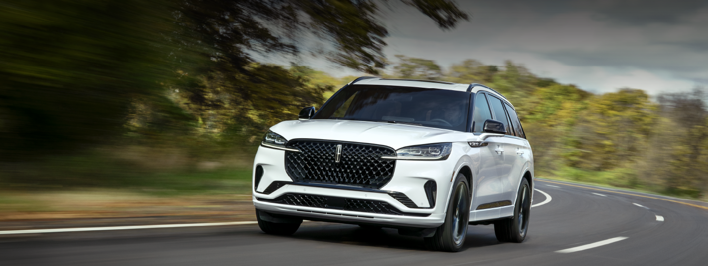 A white 2025 Lincoln Aviator® SUV is being driven down a road lined with trees. | Parks Lincoln of Wesley Chapel in Wesley Chapel FL
