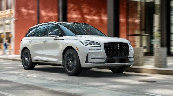A white 2025 Lincoln Corsair® SUV with the Jet Appearance Package is being driven through a city.| Parks Lincoln of Wesley Chapel in Wesley Chapel FL