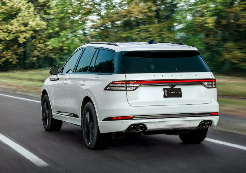 A white 2026 Lincoln Aviator® SUV is being driven away down a road lined with colorful trees. | Parks Lincoln of Wesley Chapel in Wesley Chapel FL