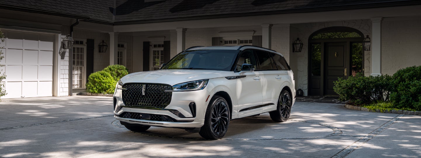 A white 2026 Lincoln Aviator® SUV is parked in the driveway of a luxury home. | Parks Lincoln of Wesley Chapel in Wesley Chapel FL