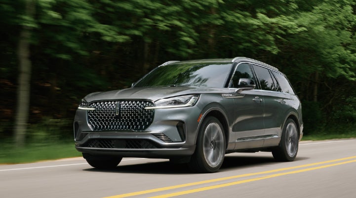 A 2027 Lincoln Aviator® SUV is being driven down a road lined with trees. | Parks Lincoln of Wesley Chapel in Wesley Chapel FL